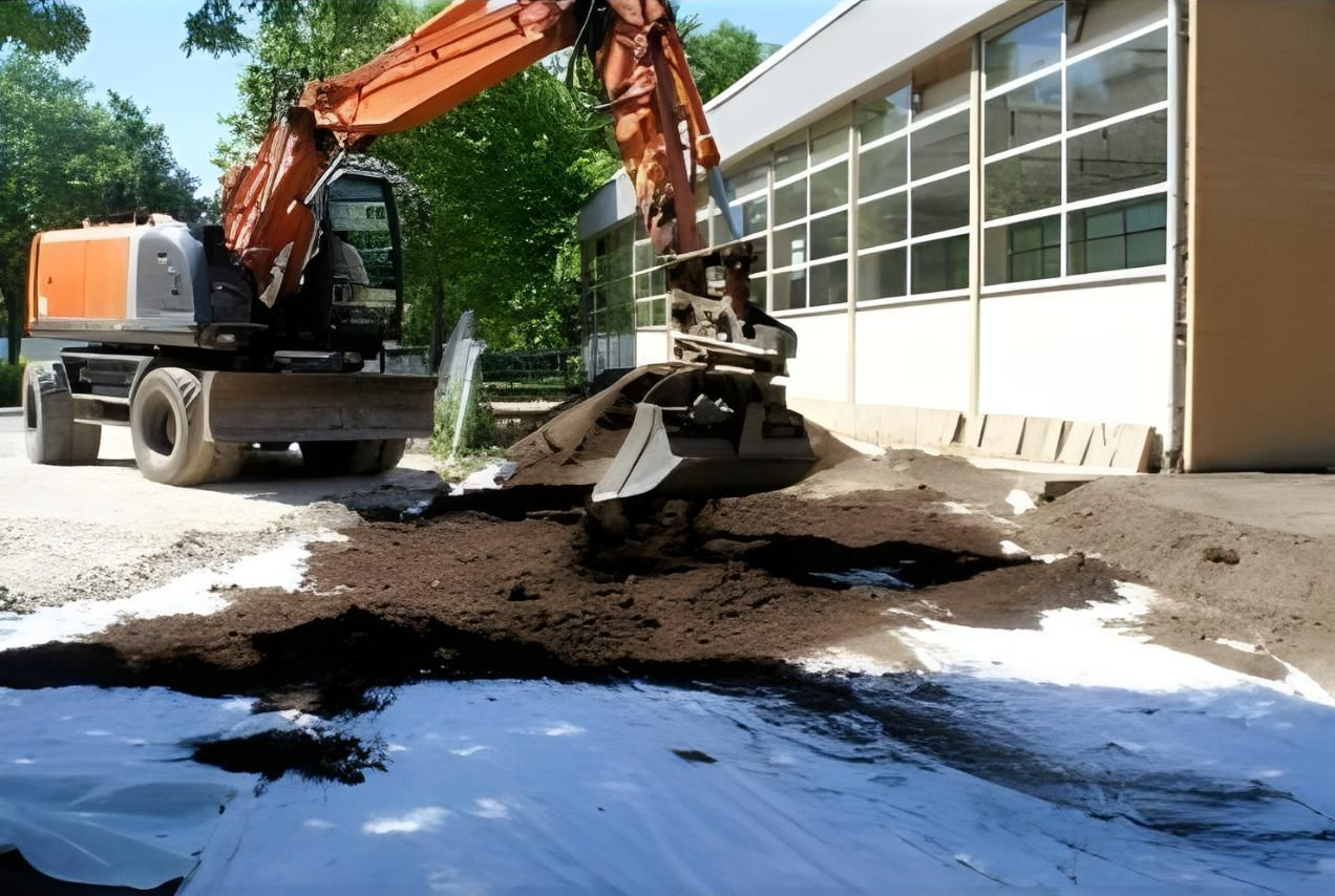 An Excavator is Digging a Hole in the Ground in Front of a Building — Husky Demolition In Heatherbrae, NSW