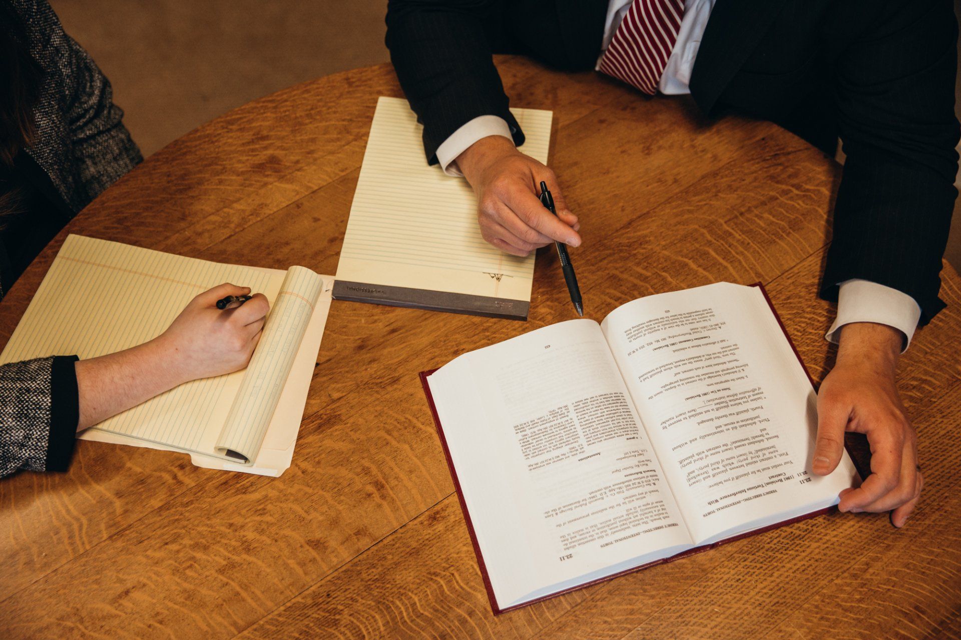Three people at a wooden table reviewing papers and an open document together.