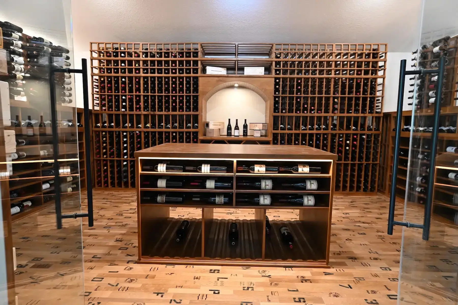 Wine cellar with wooden racks, a central tasting table, and shelving in a warmly lit room
