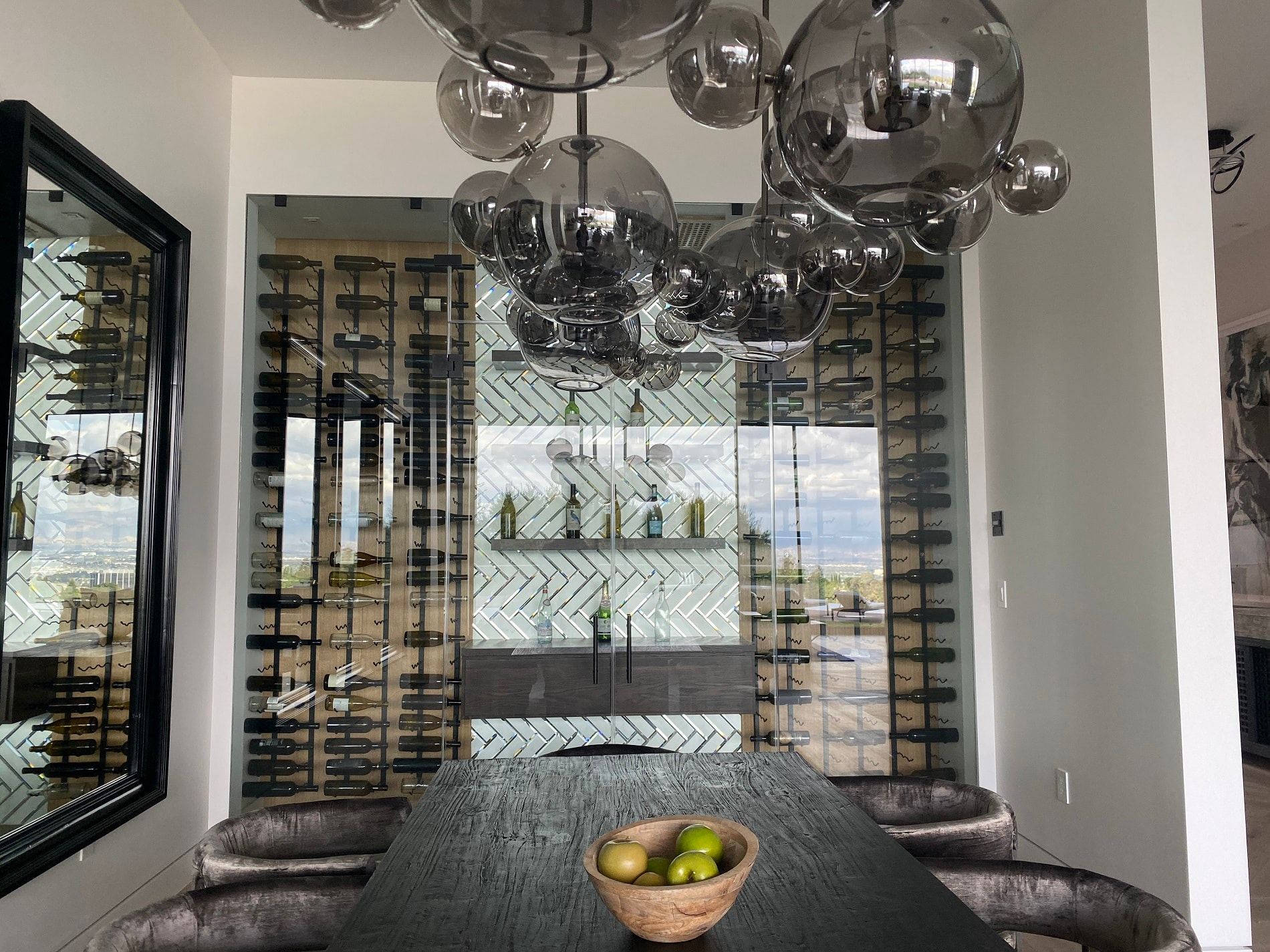 Modern dining room with a glass table, wine racks, and metallic pendant lights reflected in mirrors