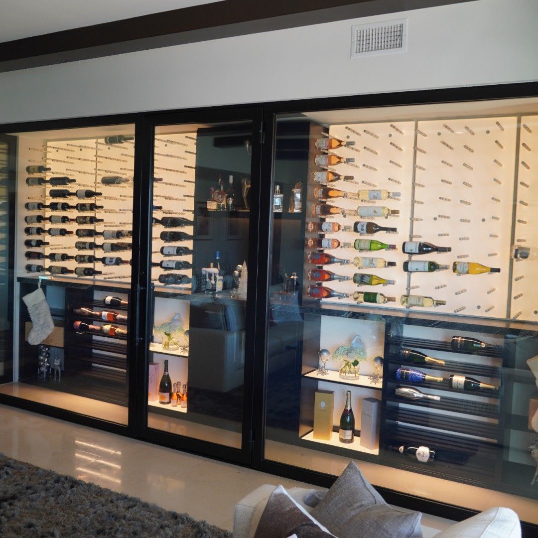 Wine display in a glass-fronted cabinet with neatly arranged bottles and stemware in a modern room