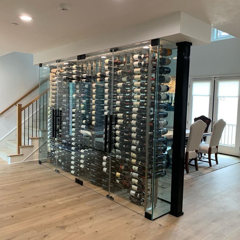 Glass wine display wall in a modern home dining area with staircase and wood floors.