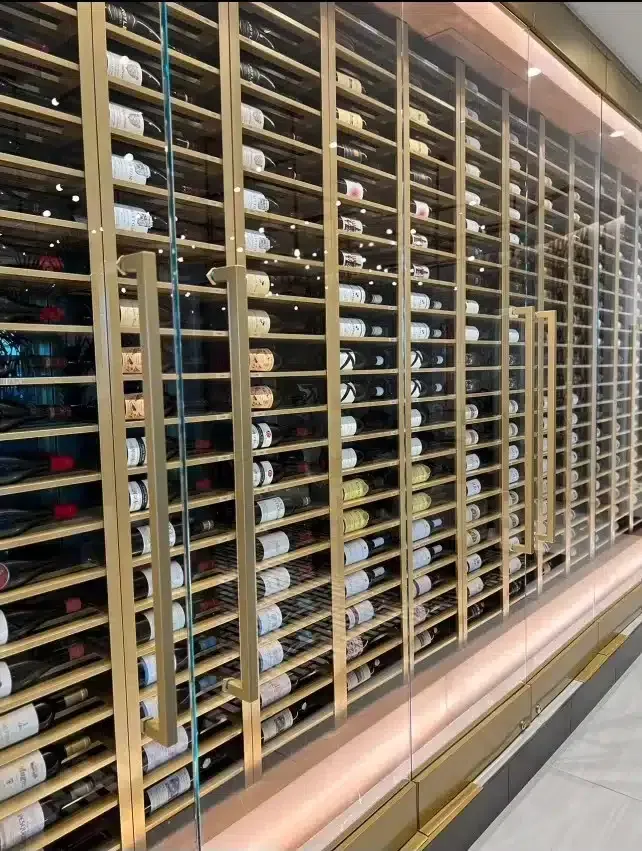 Glass wine storage wall with rows of bottles behind wooden slats in a modern interior
