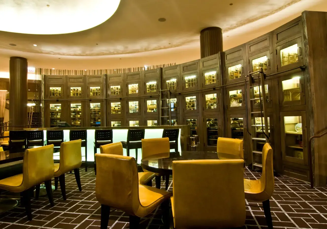 Elegant library lounge with yellow chairs, tables, and illuminated bookshelves in a circular room