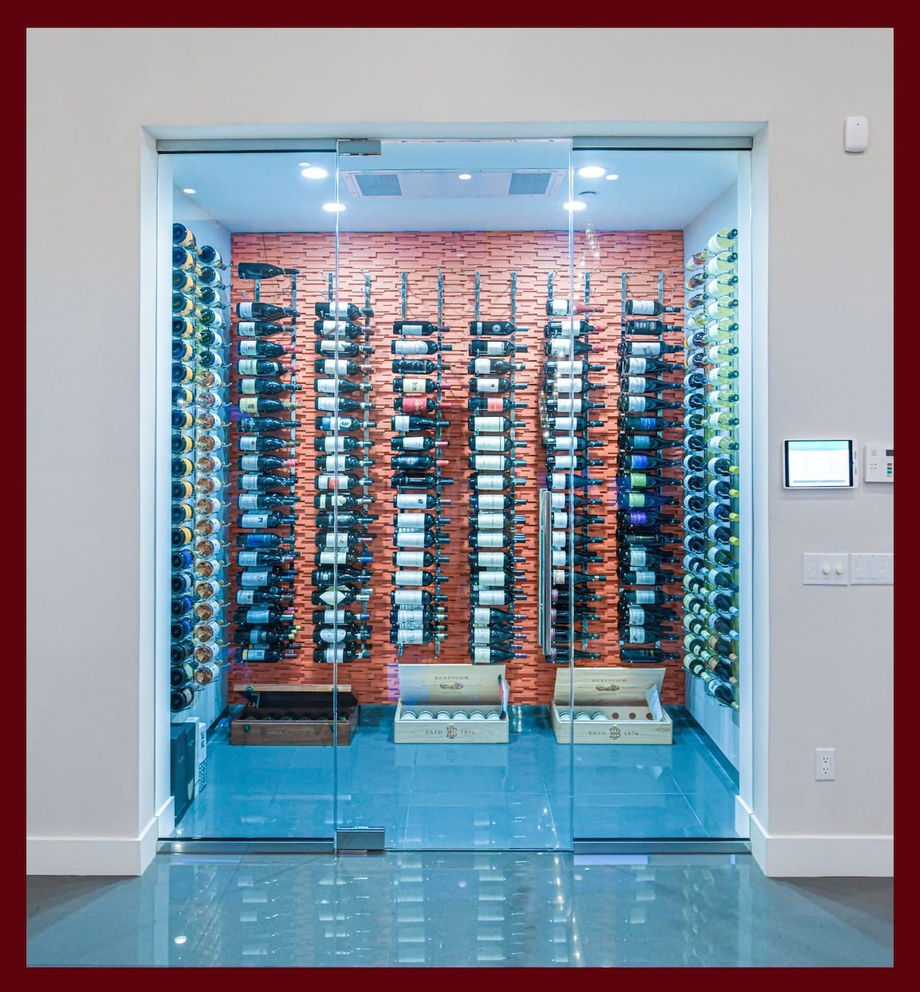 Glass wine cellar with rows of bottles behind a clear door in a modern interior