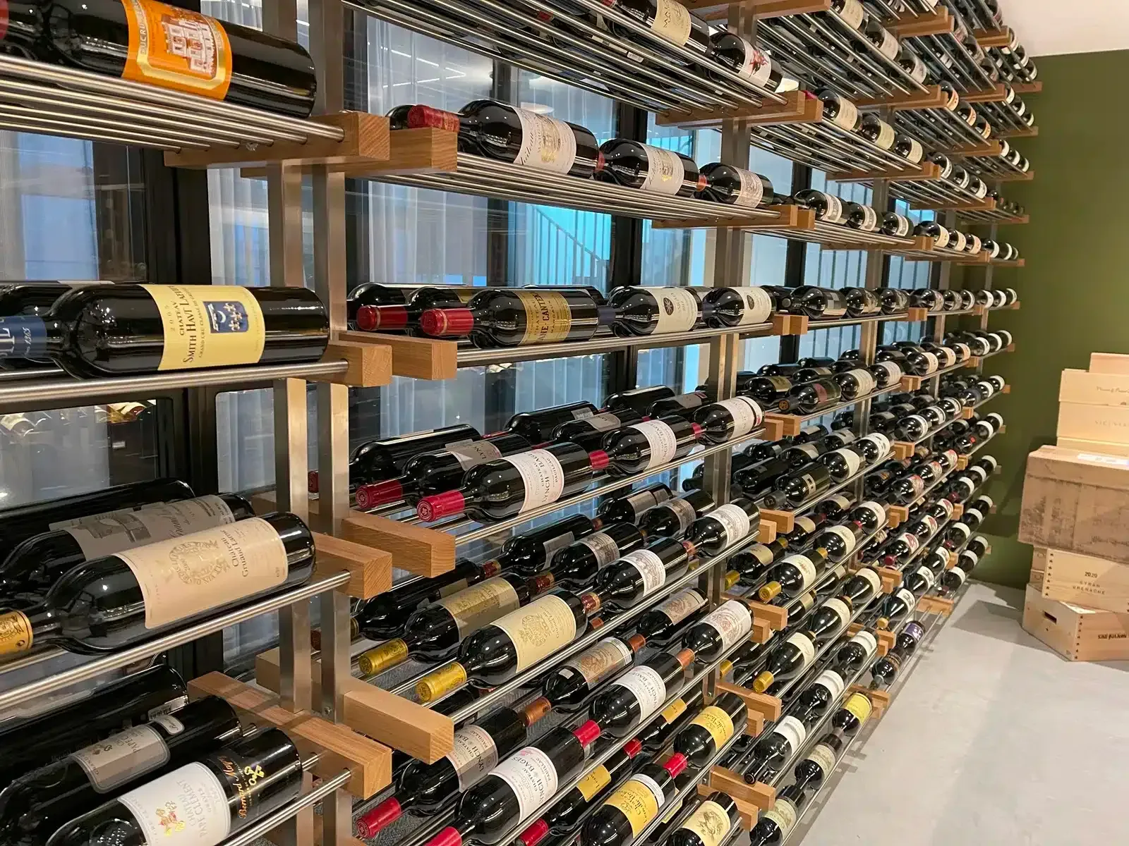 Wine bottles stored on wall-mounted racks in a shop cellar, with cardboard boxes stacked nearby.