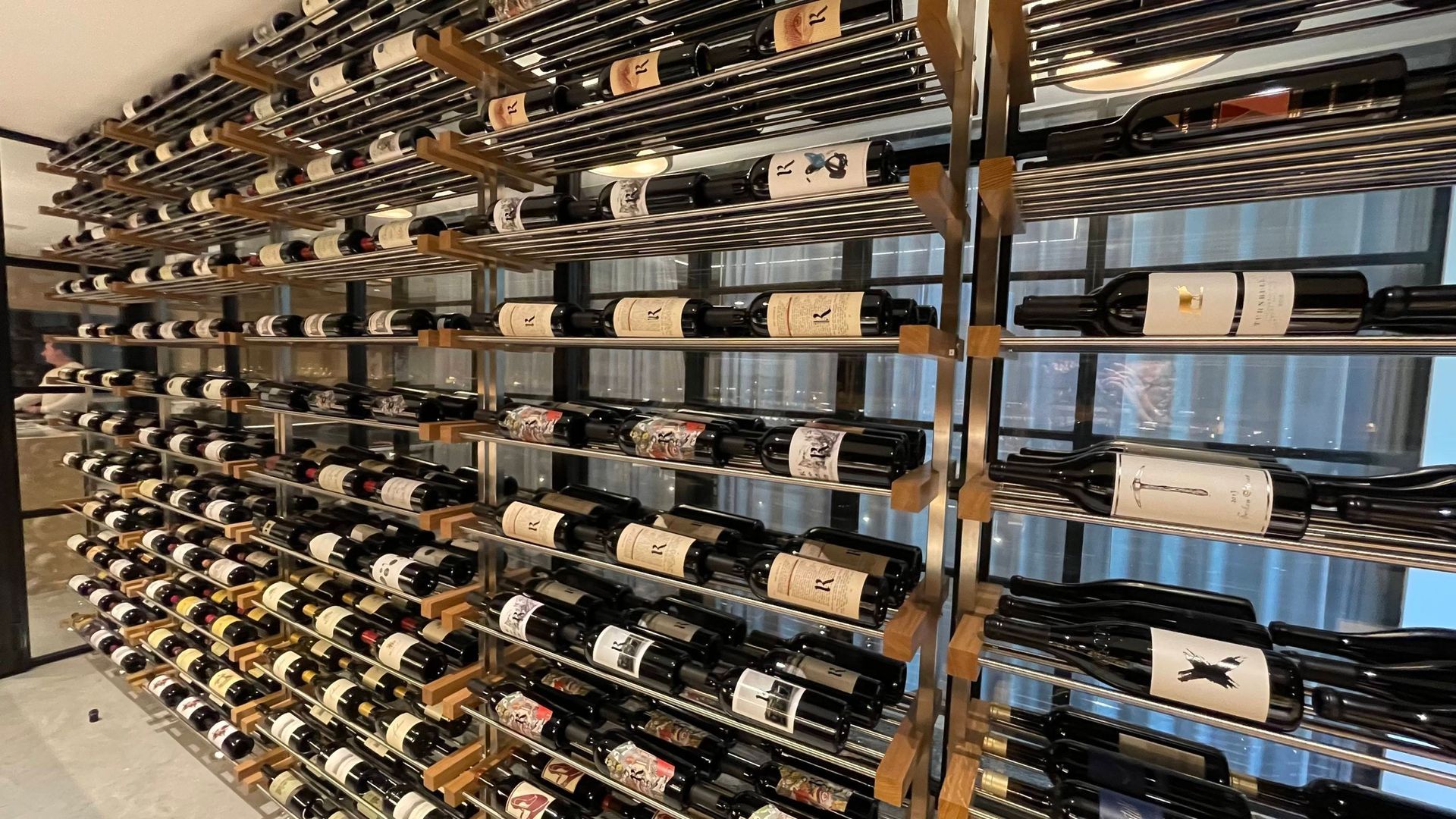 Rows of wine bottles stored horizontally on metal racks in a cellar or wine storage room.