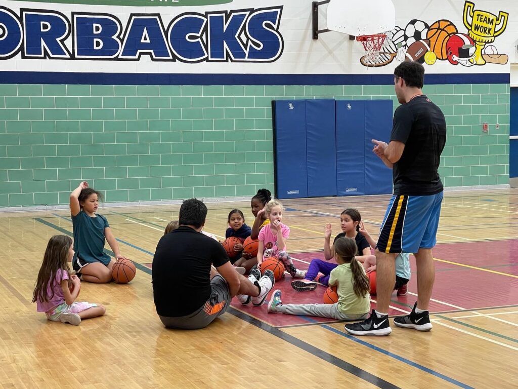 Coach talking to children seated on a gym floor during a group activity