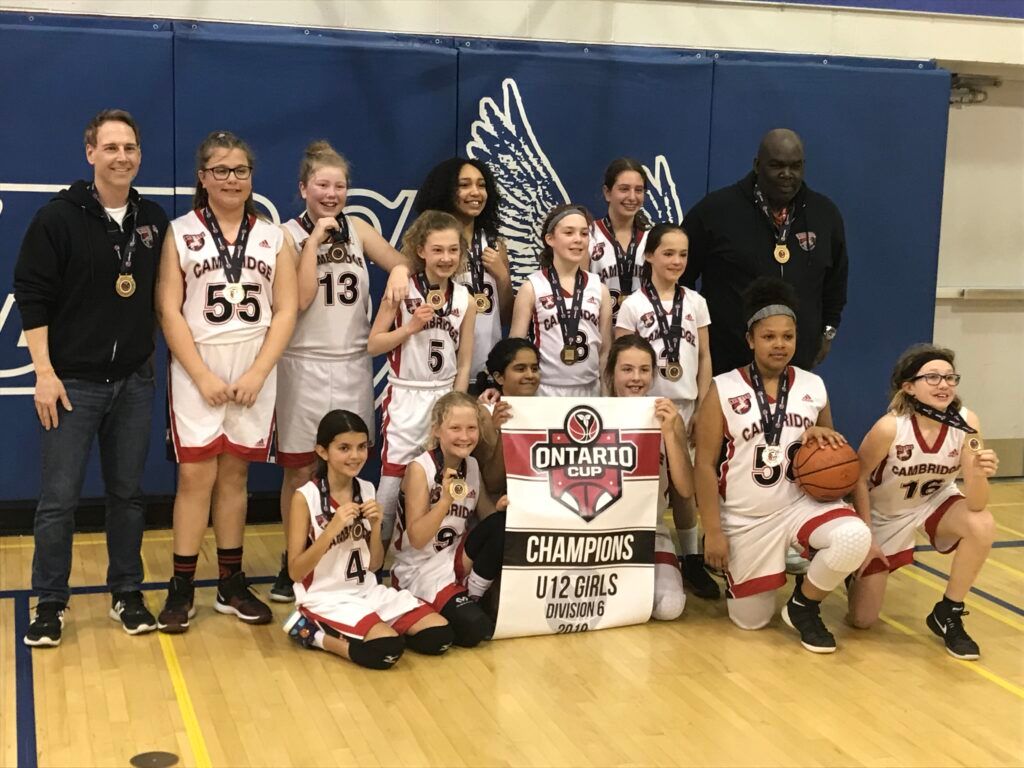 Youth basketball team posing with championship trophy on gym floor, with coaches standing behind them