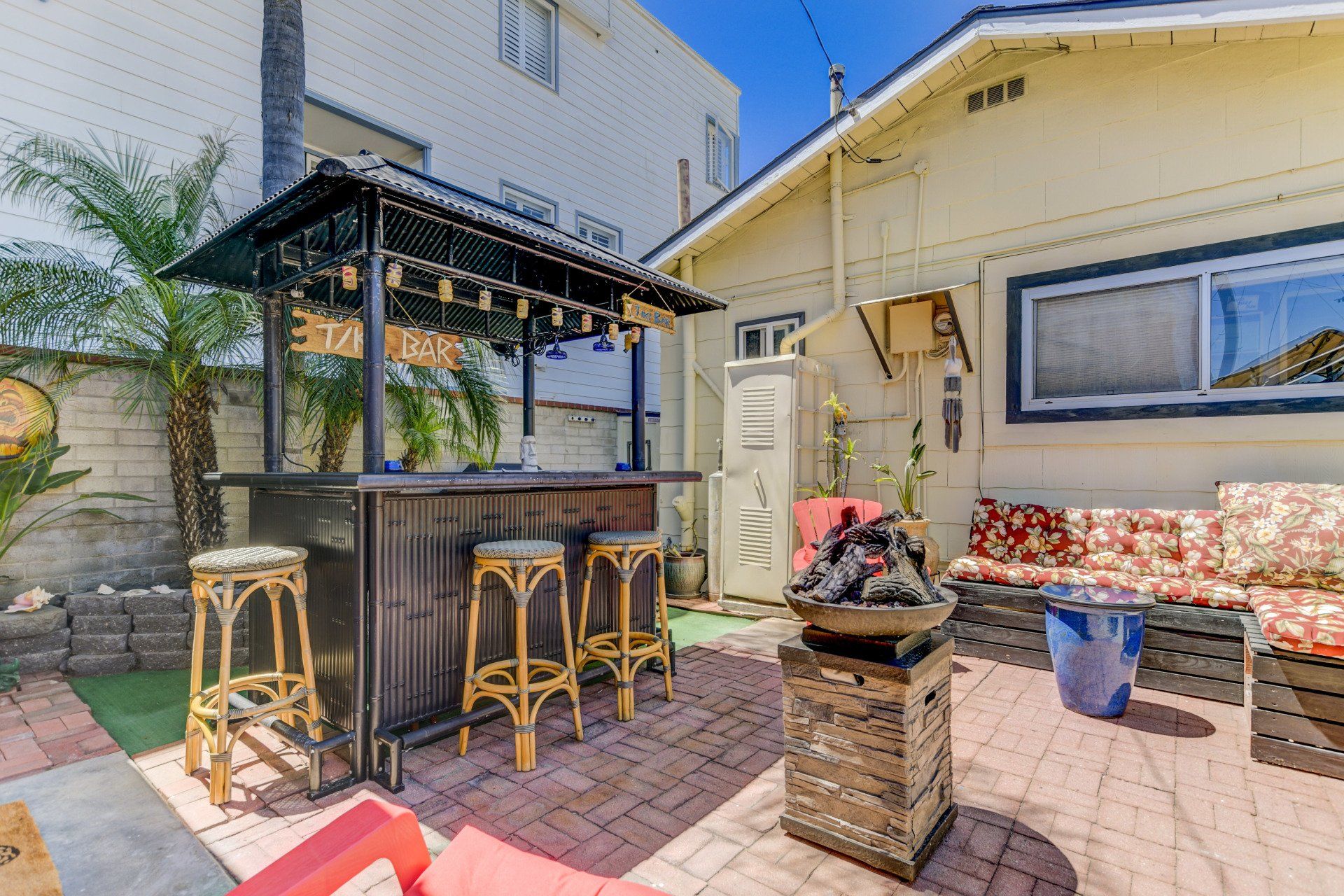 Outdoor bar with stools, fire pit, and seating area in a backyard setting.