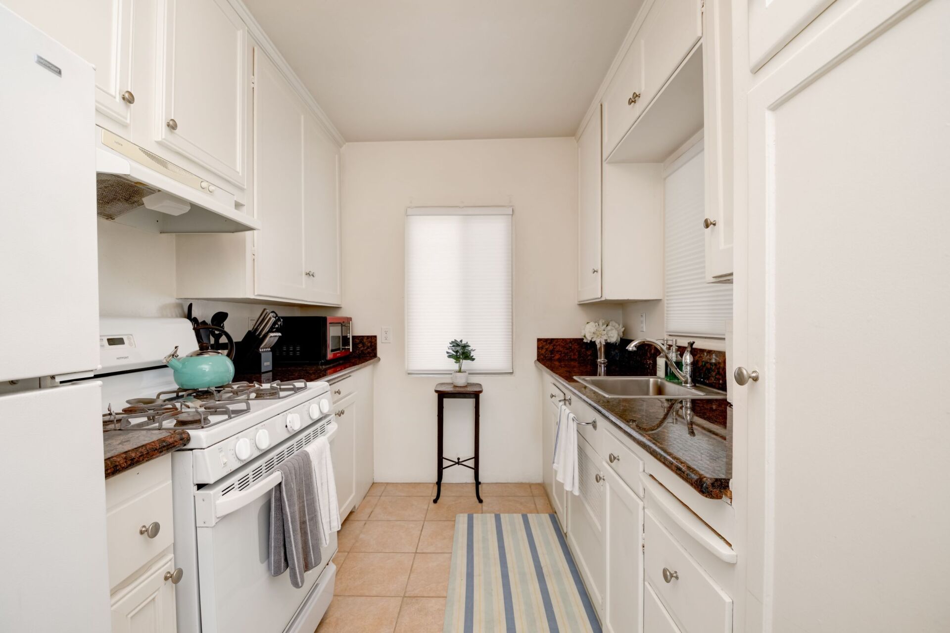 A kitchen with white cabinets , a stove , a refrigerator , a sink and a window.