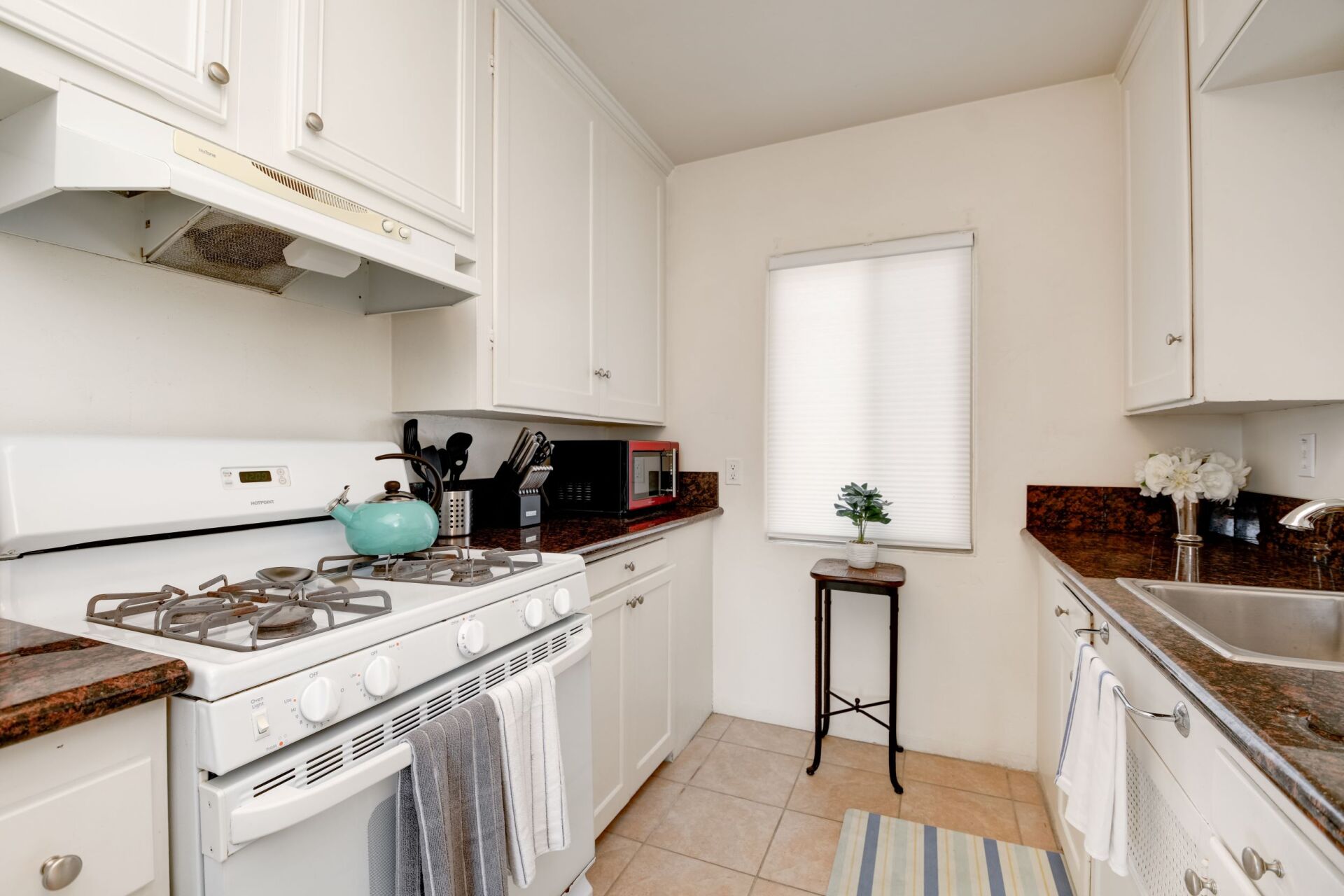 A kitchen with white cabinets , a stove , a sink , and a window.