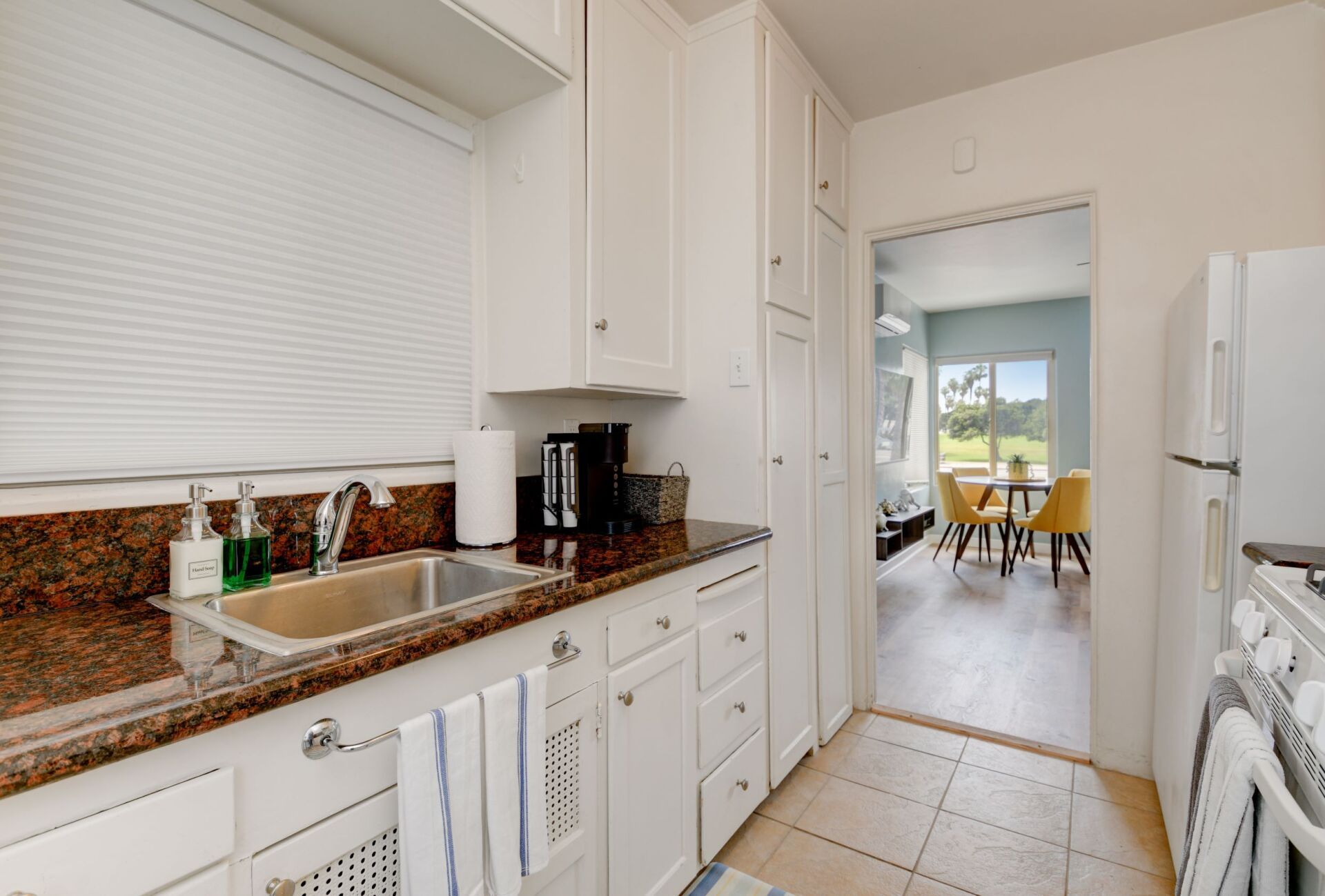 A kitchen with white cabinets , granite counter tops , a sink and a refrigerator.