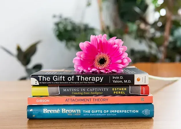 Stack of therapy books with a pink flower on top against a blurred indoor background