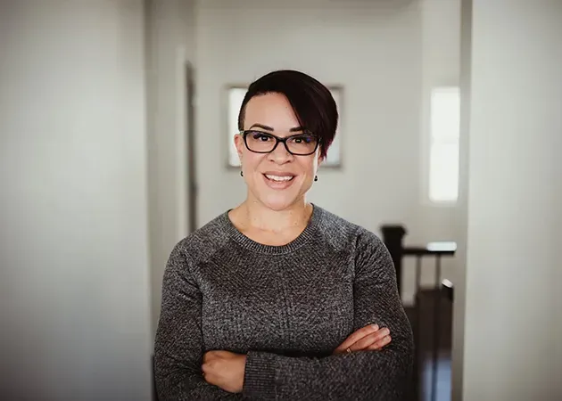 Smiling person in glasses with arms crossed in a bright hallway