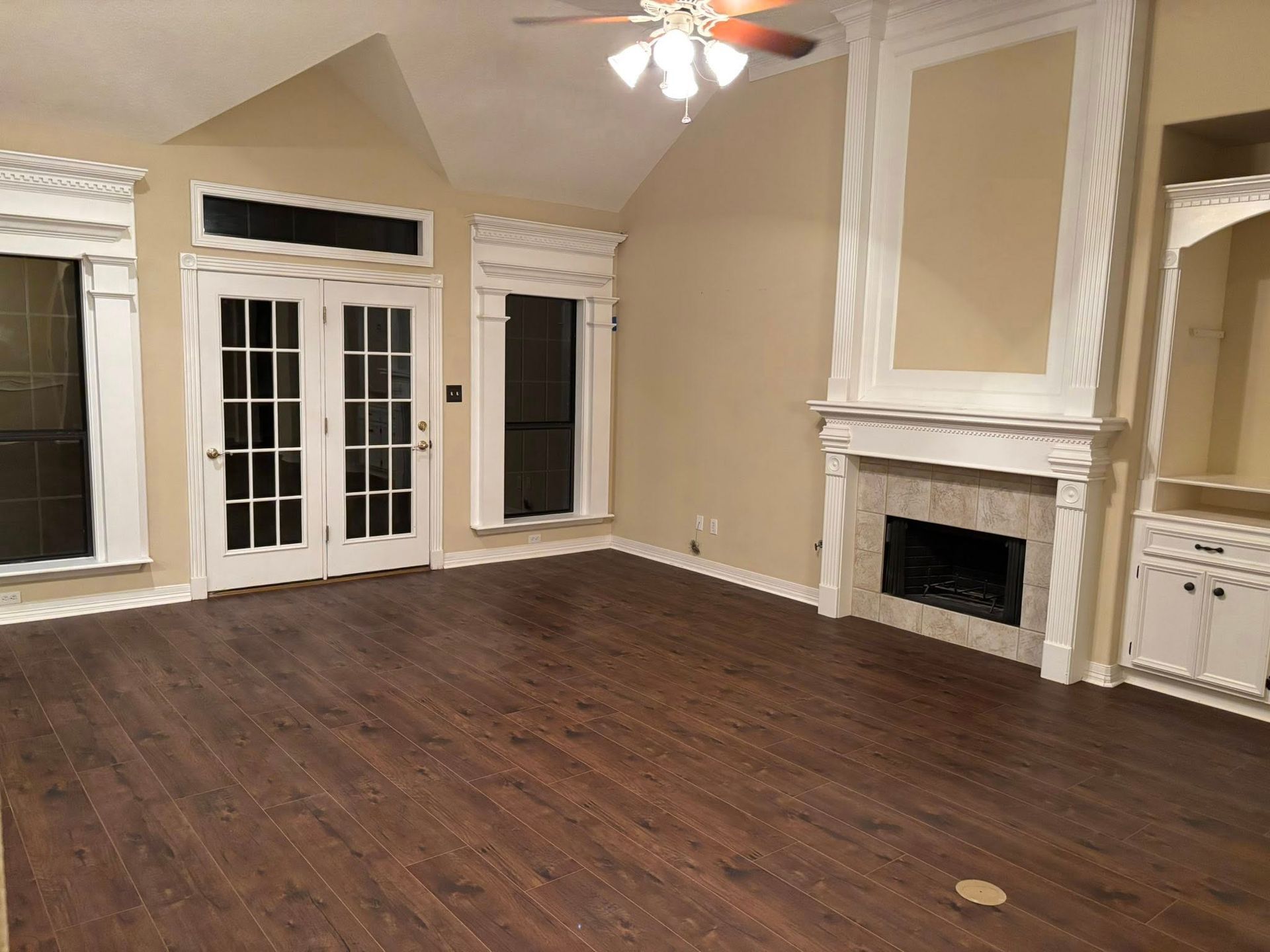 Empty living room with hardwood floors, fireplace, French doors, and ceiling fan in beige walls
