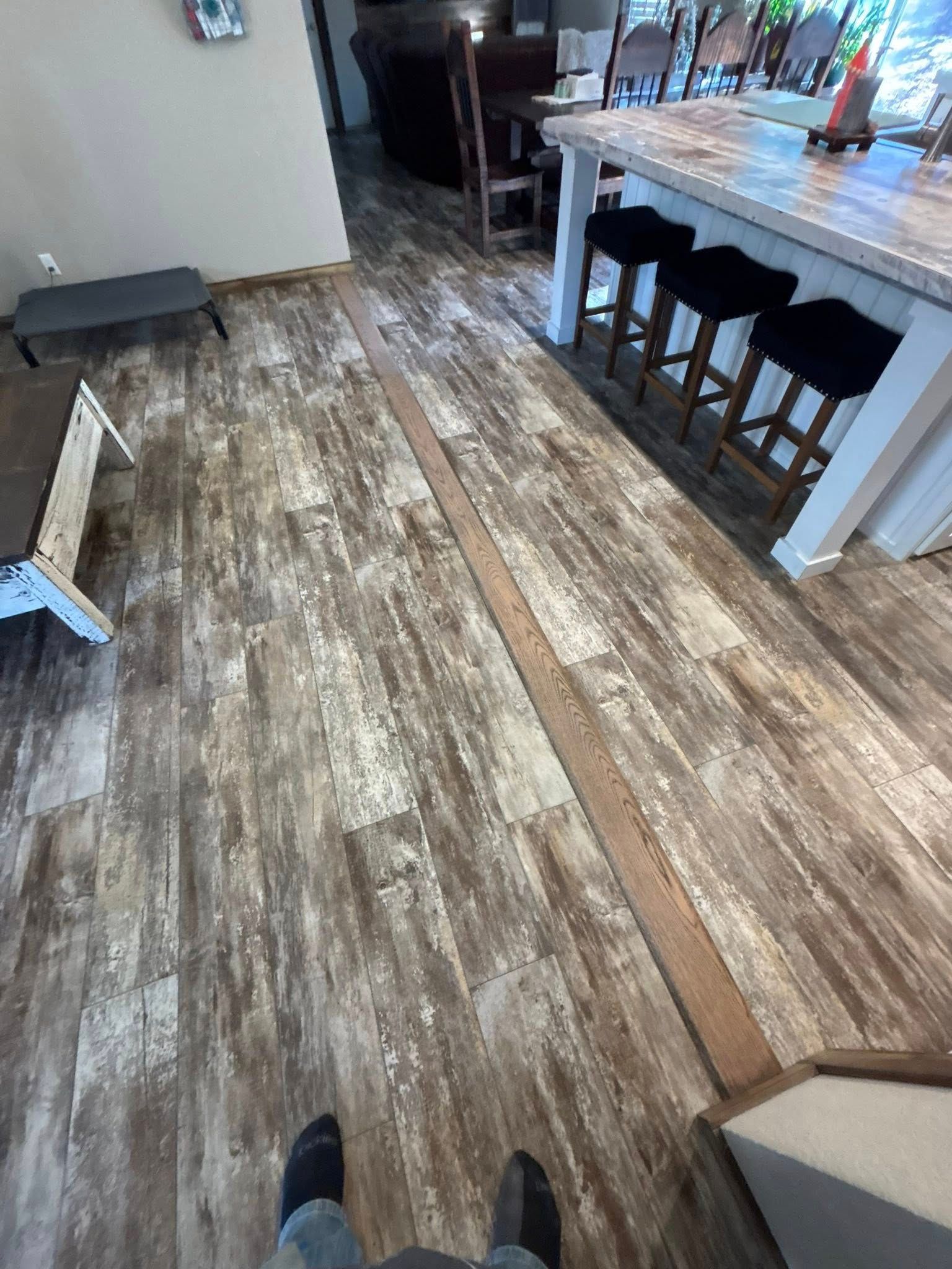 Wood-look floor in a kitchen or dining area with a white island, bar stools, and a hallway beyond.