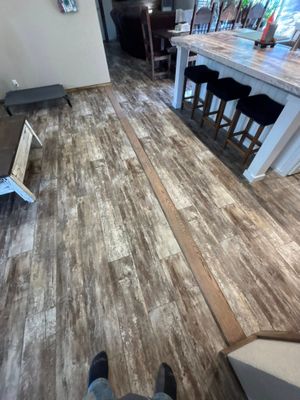 Wood-look floor in a kitchen or dining area with a white island, bar stools, and a hallway beyond.