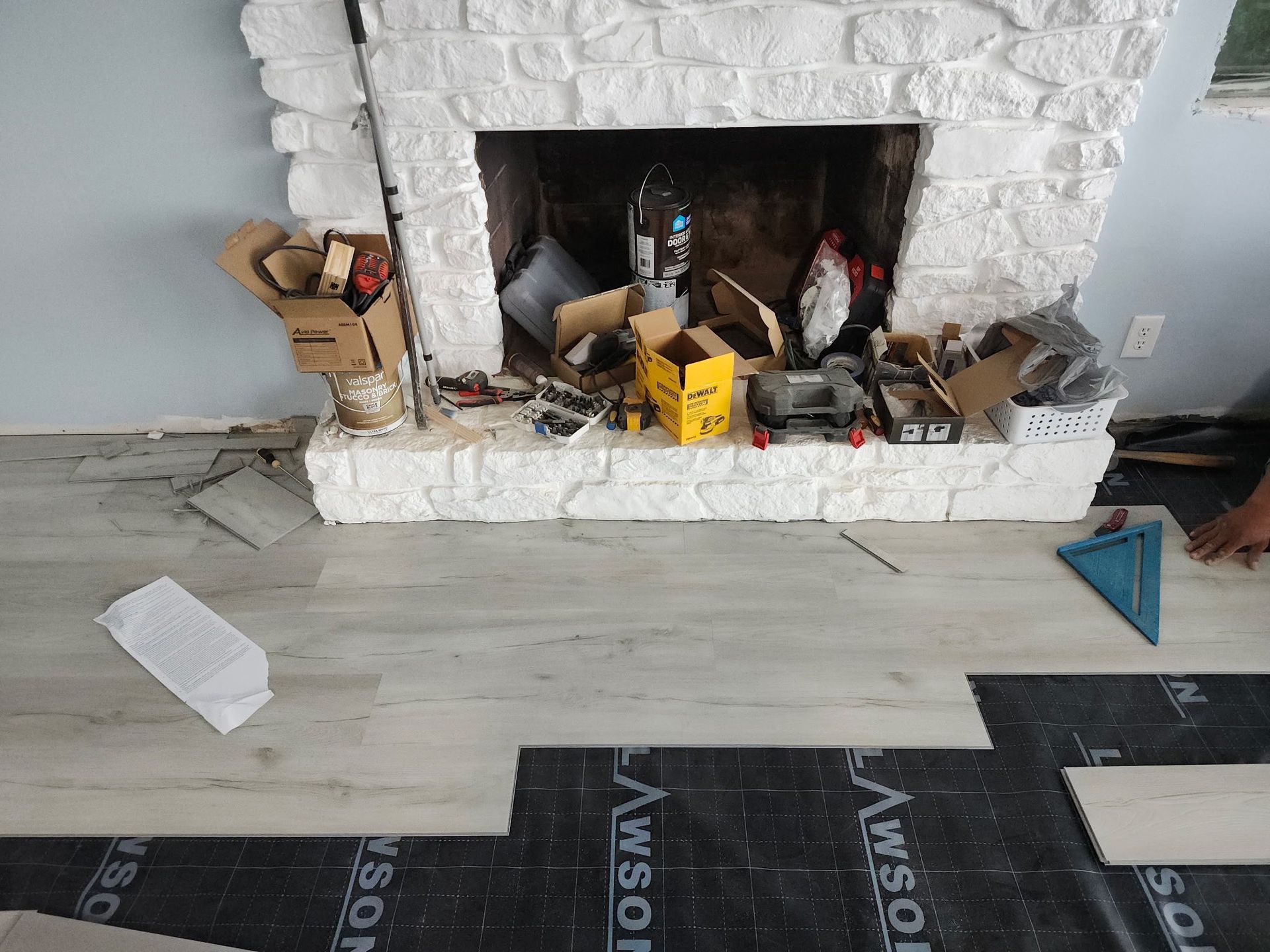 Messy fireplace with tools and debris on a light wood floor in an unfinished room