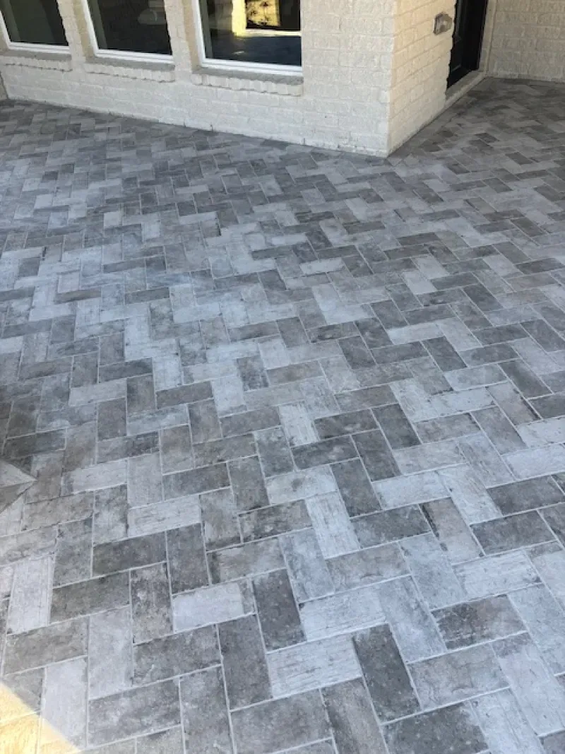 Gray paver patio beside a beige house exterior and window