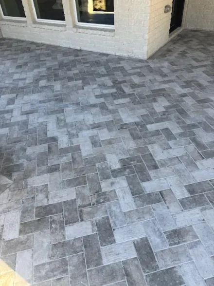 Gray paver patio beside a beige house exterior and window