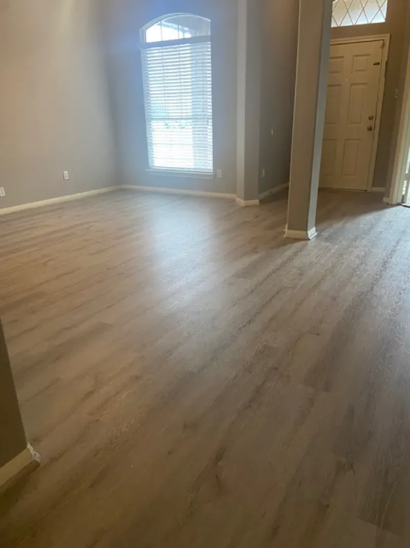 Empty beige living room with wood flooring, arched window, and open doorway to a closet