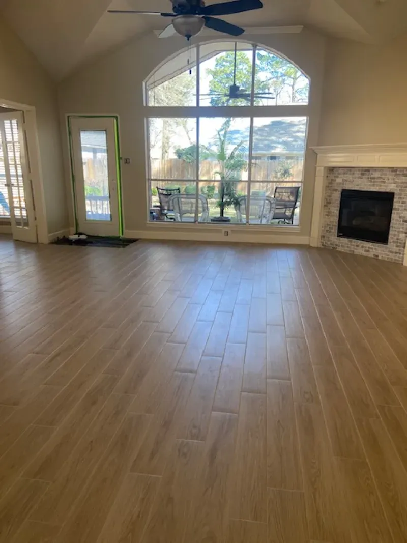 Spacious living room with wood floors, large arched window, ceiling fan, and stone fireplace