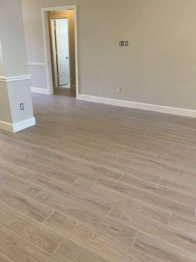 Empty room with light wood flooring, beige walls, and an open doorway to a lit hall.