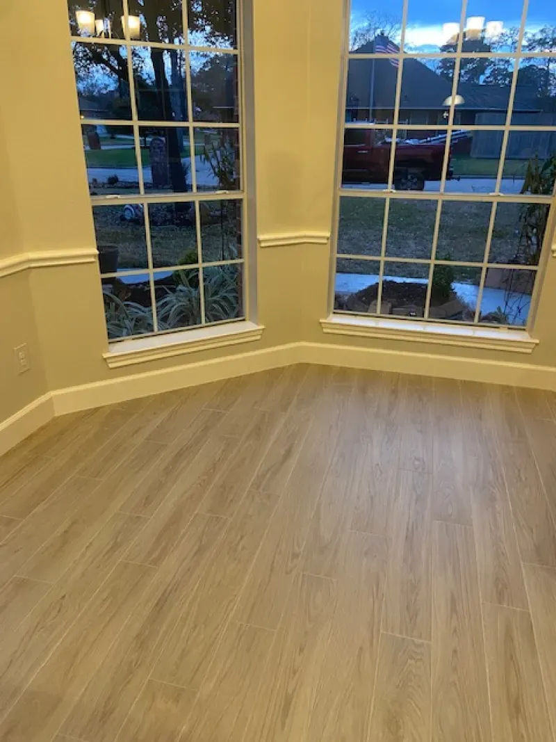 Empty room with light wood flooring, bay windows, and evening light outside