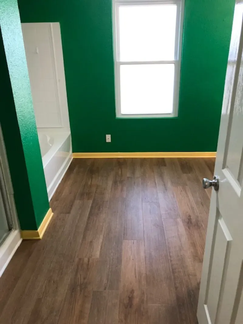 Empty room with green walls, wood floor, white window, and open door