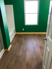 Empty room with green walls, wood floor, white window, and open door
