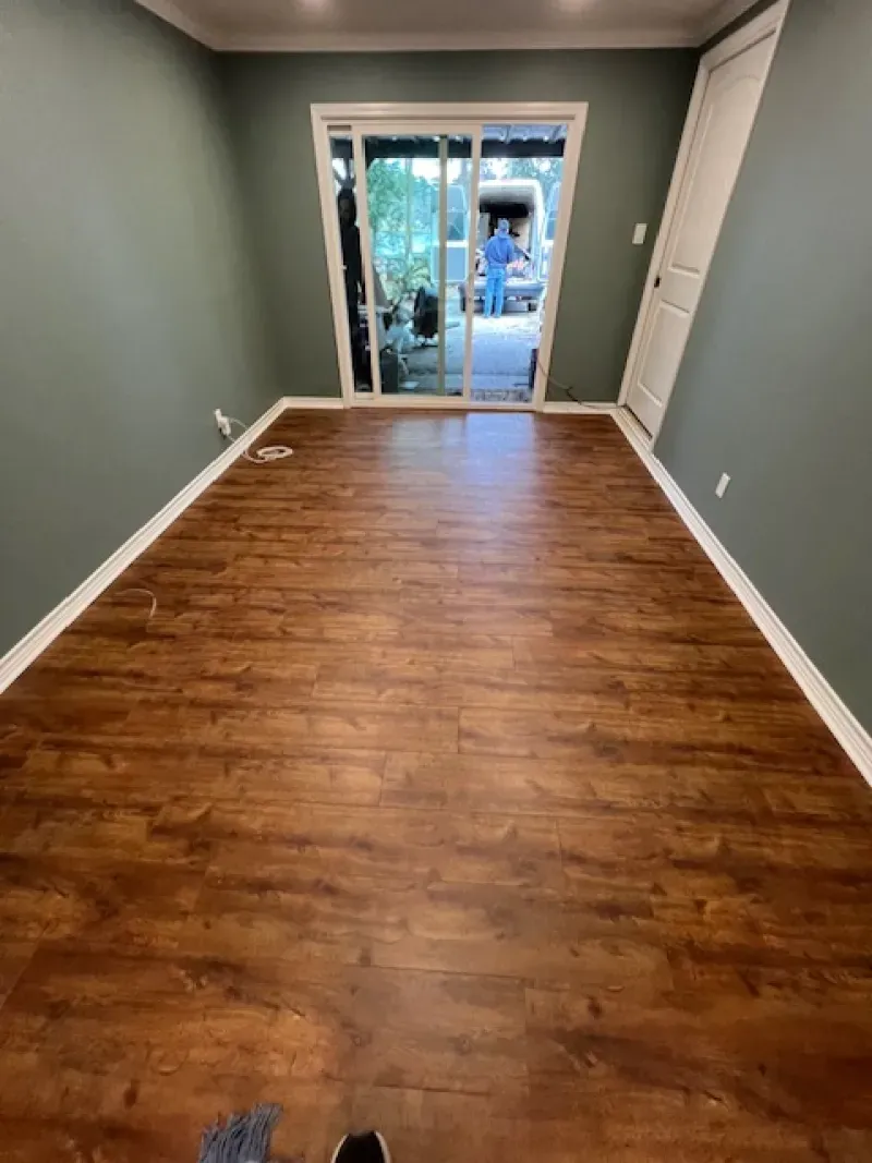 Empty narrow room with wood floors and gray walls, facing sliding glass doors at the far end.
