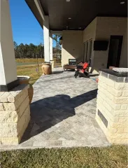 Covered patio with stone floor, porch columns, and a red chair overlooking a grassy yard