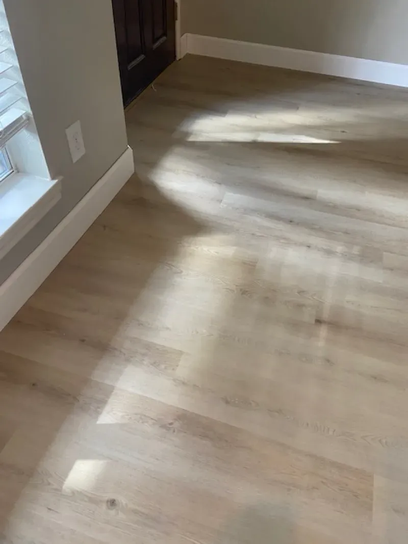 Sunlit hardwood floor in an empty room with white baseboards and a doorway at the back