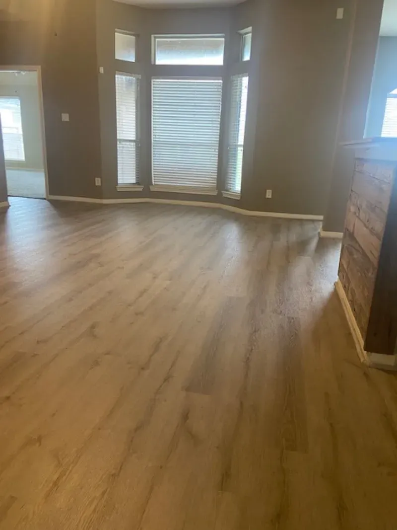 Empty living room with light wood floors and large windows and sliding glass doors at the back.