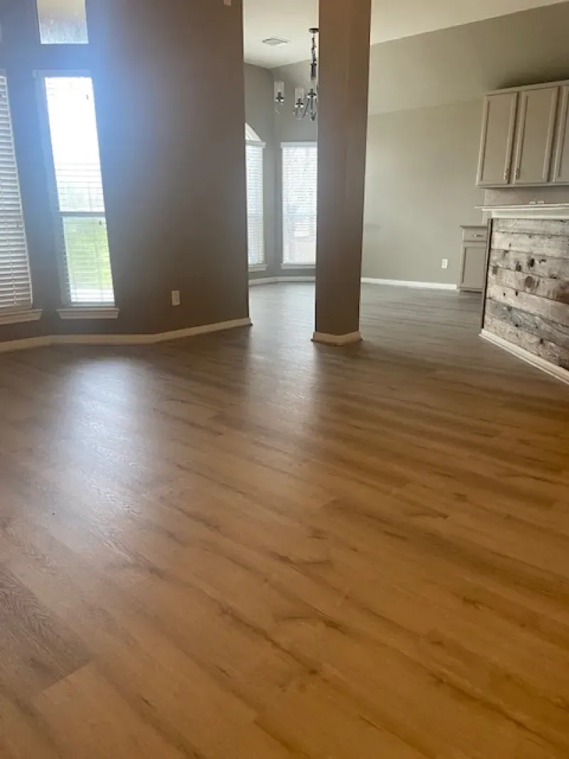 Empty living room with hardwood floors, tall windows, beige walls, and a white dresser by the wall
