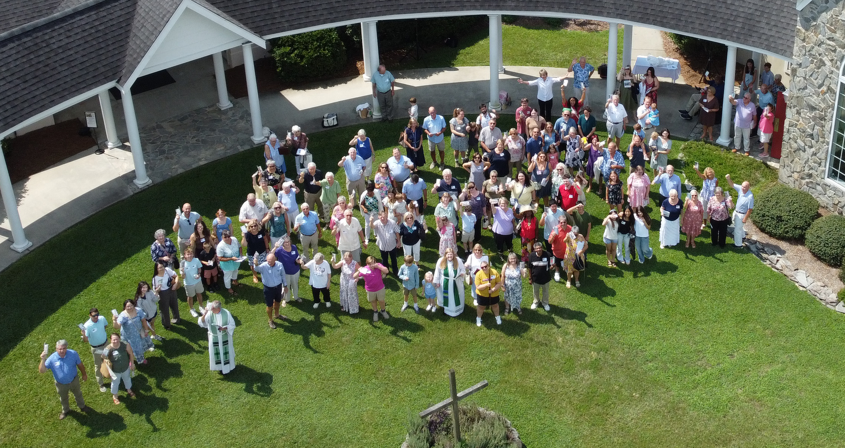 People holding up colorful papers, looking upward in a sunny outdoor setting near a building.