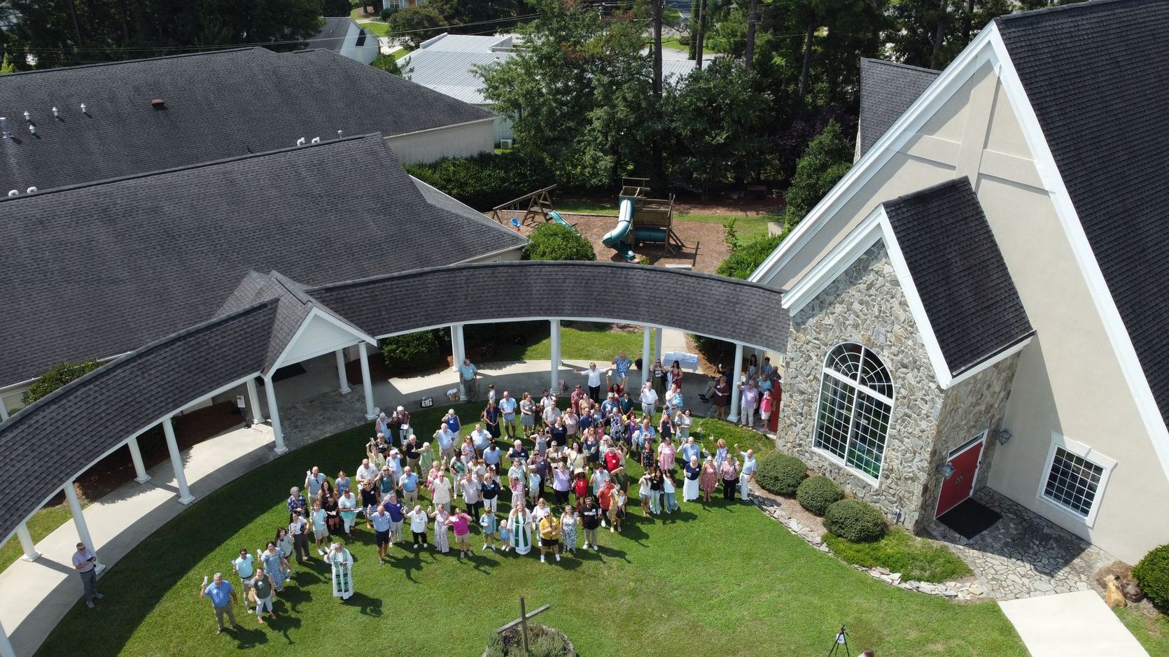 People holding up colorful papers, looking upward in a sunny outdoor setting near a building.