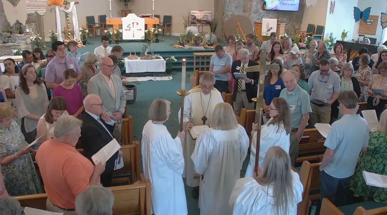 Church congregation standing in a semicircle listening to the Gospel read during a service