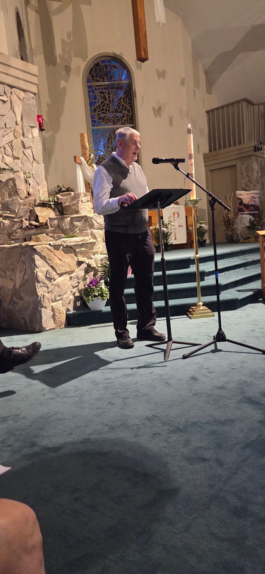 Person reading from a podium in a church, with a microphone and ornate stone backdrop.