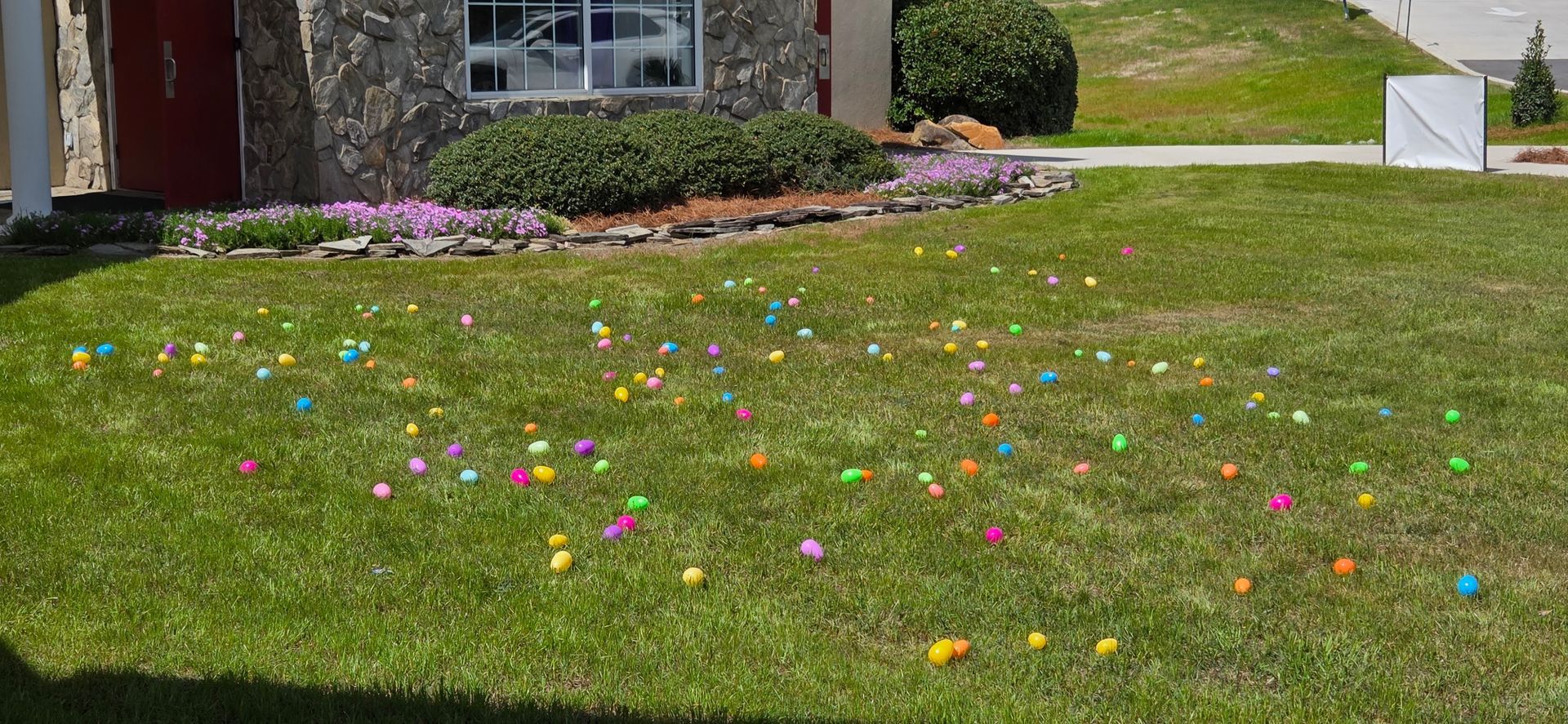 Lawn scattered with colorful Easter Eggs in front of a house and garden bed