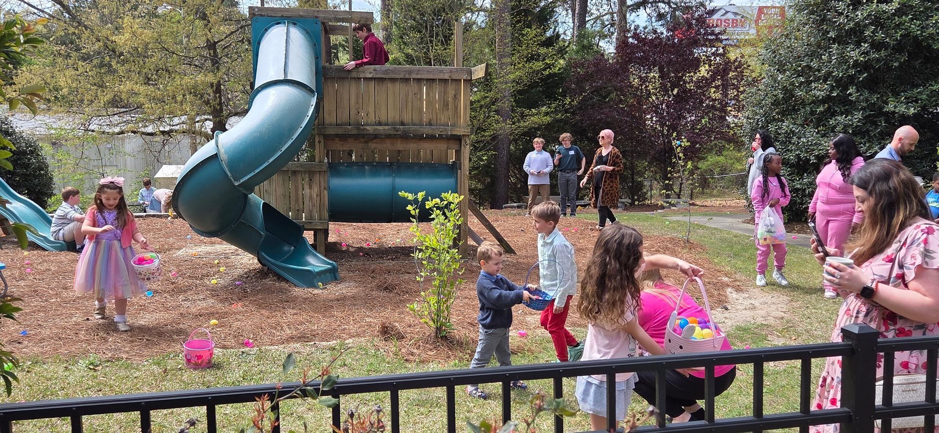 Children playing in a park near a blue spiral slide and small flower petals scattered on the ground