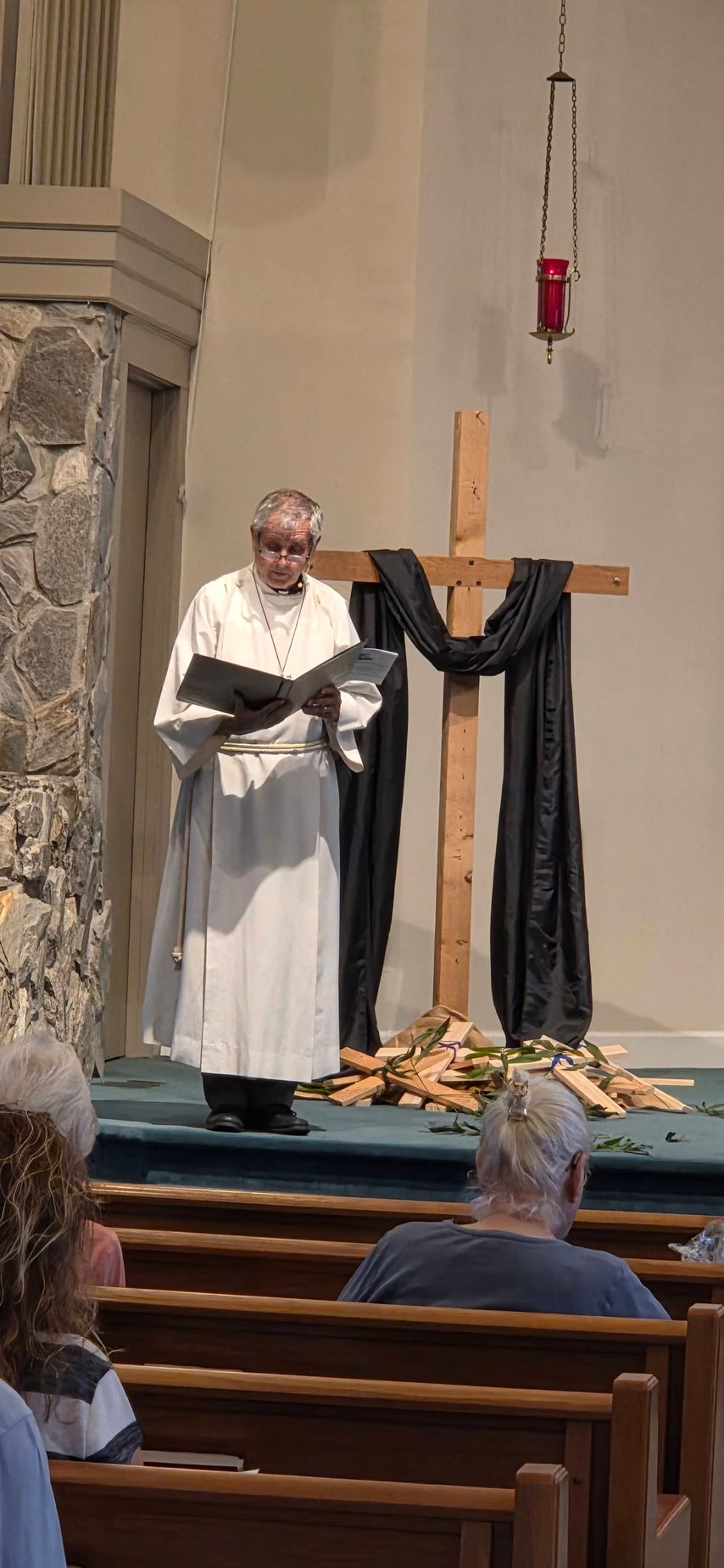 Priest reading at a church altar draped in black, with a wooden cross and flowers below.