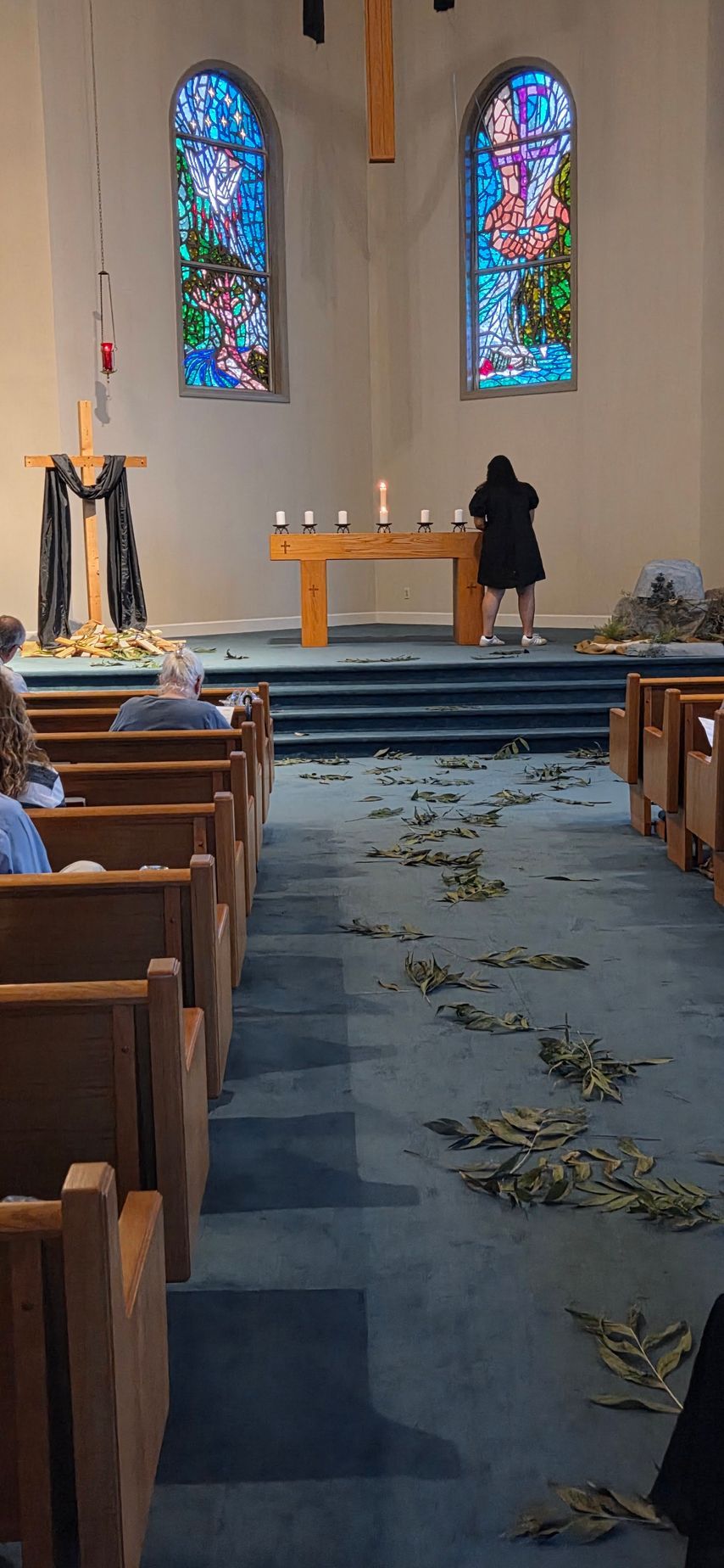 Church sanctuary with altar, stained-glass windows, and pews with leafy debris on the aisle.