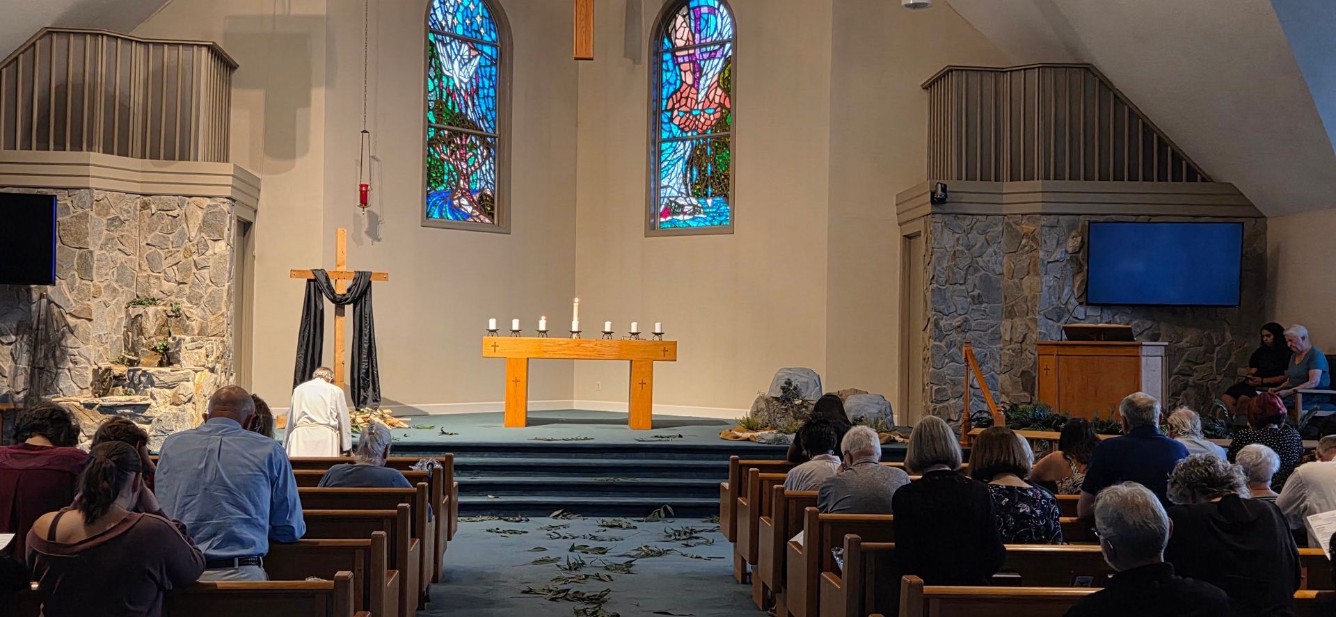 Church sanctuary with people seated in pews facing the altar and stained-glass windows.