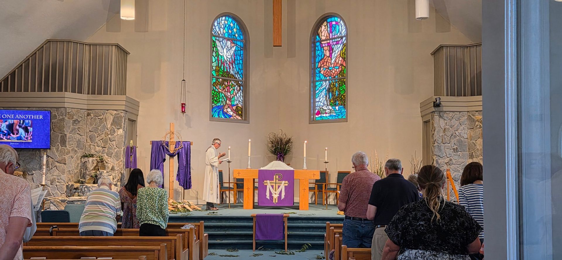 Church sanctuary with stained-glass windows, altar, and congregation seated facing the front during a service