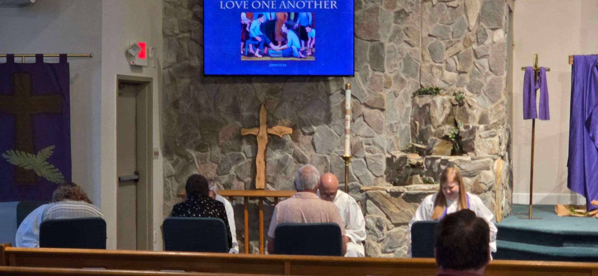 Church sanctuary with a cross and screen above people seated in pews facing the front