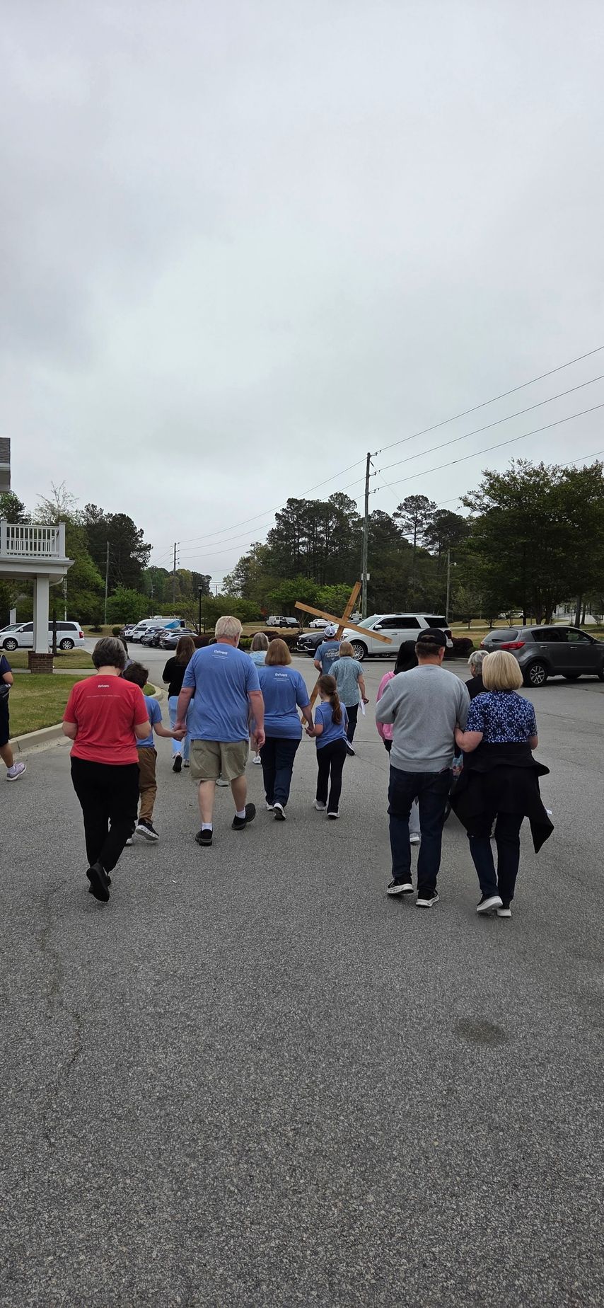 People walking down a gravel road in a cloudy neighborhood, with cars and houses nearby.