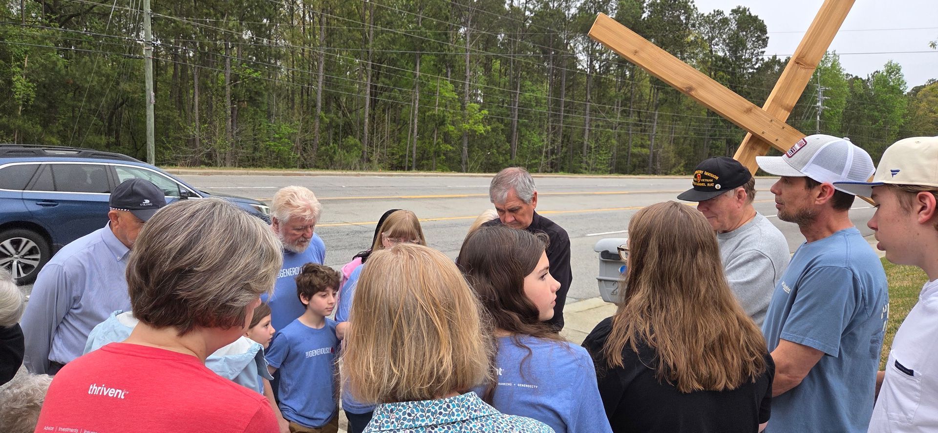 Group of people gathered outdoors near a large wooden cross at a memorial or event site