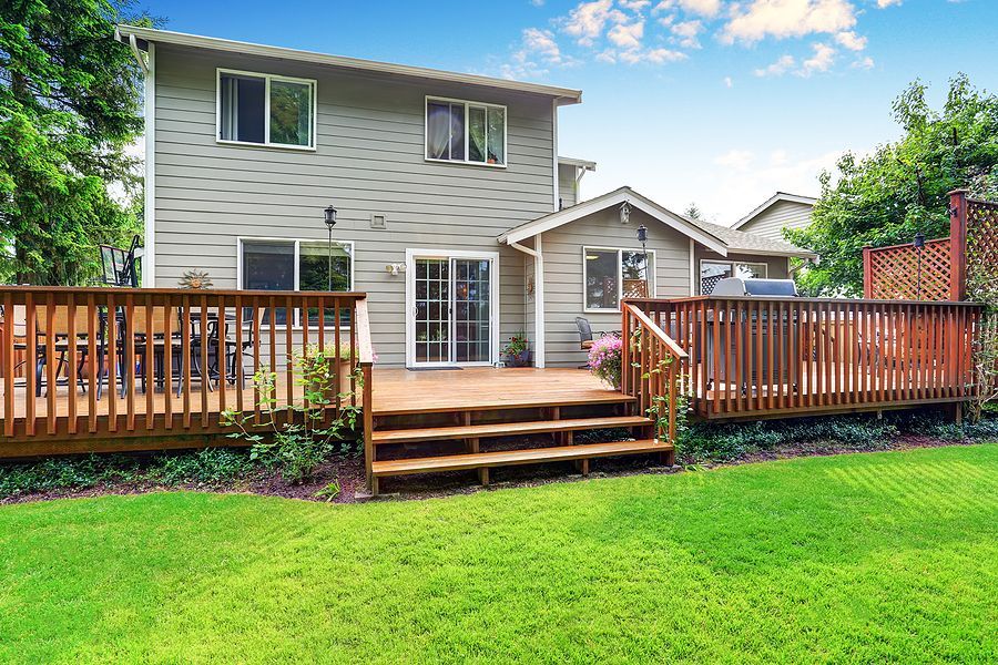 Backyard deck attached to a gray house with green lawn and stairs leading down.